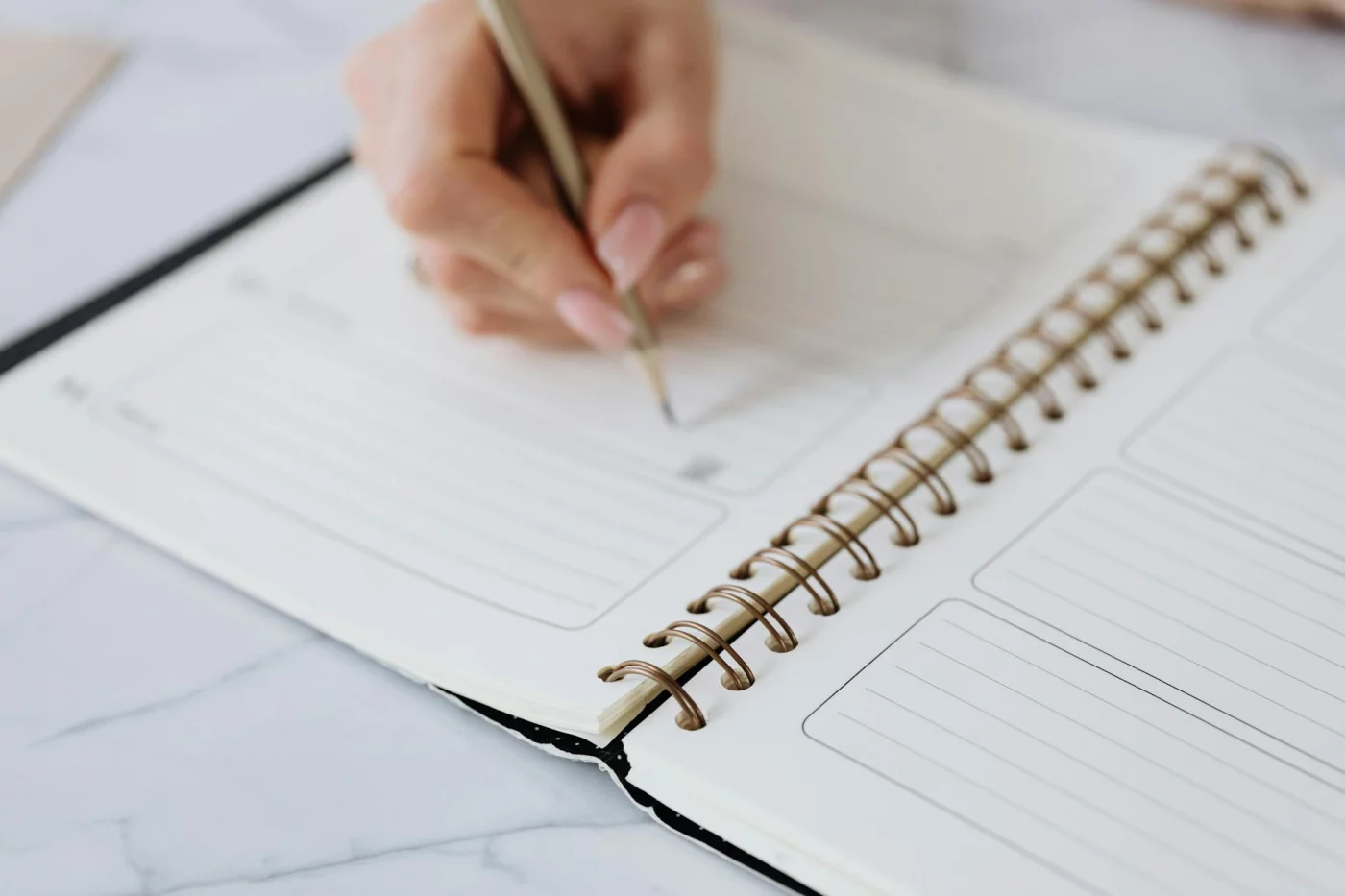 Person writing a study schedule template in a planner with a pencil on a marble surface