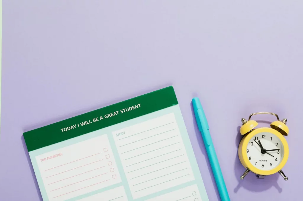 Student planner, pen, and yellow alarm clock illustrating time management tips for students on a pastel backdrop