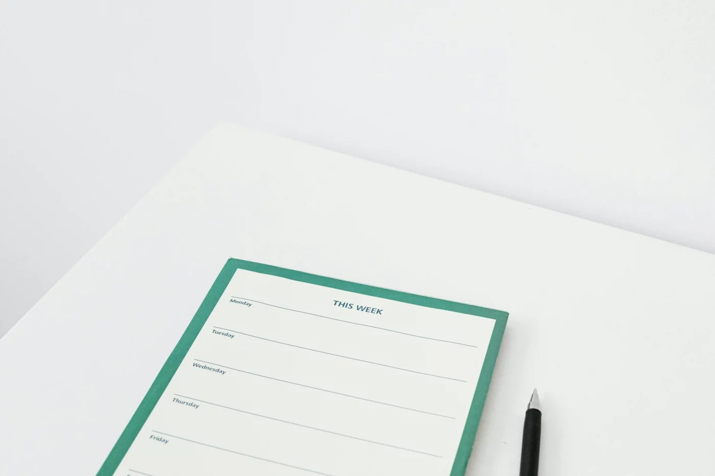 Undated weekly planner template on a white desk with a pen, showing a clean layout for flexible weekly planning