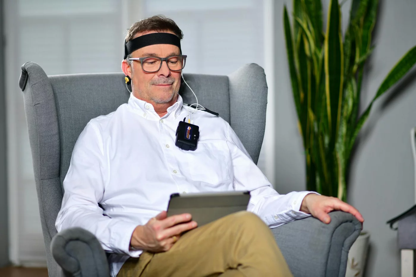 Man in an armchair using a neurofeedback device while reviewing flow neuroscience clinical trials and safety