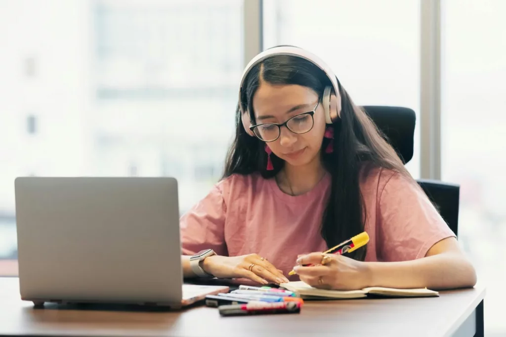 Young woman in headphones at a desk with laptop and notebook, showing how to improve focus while studying