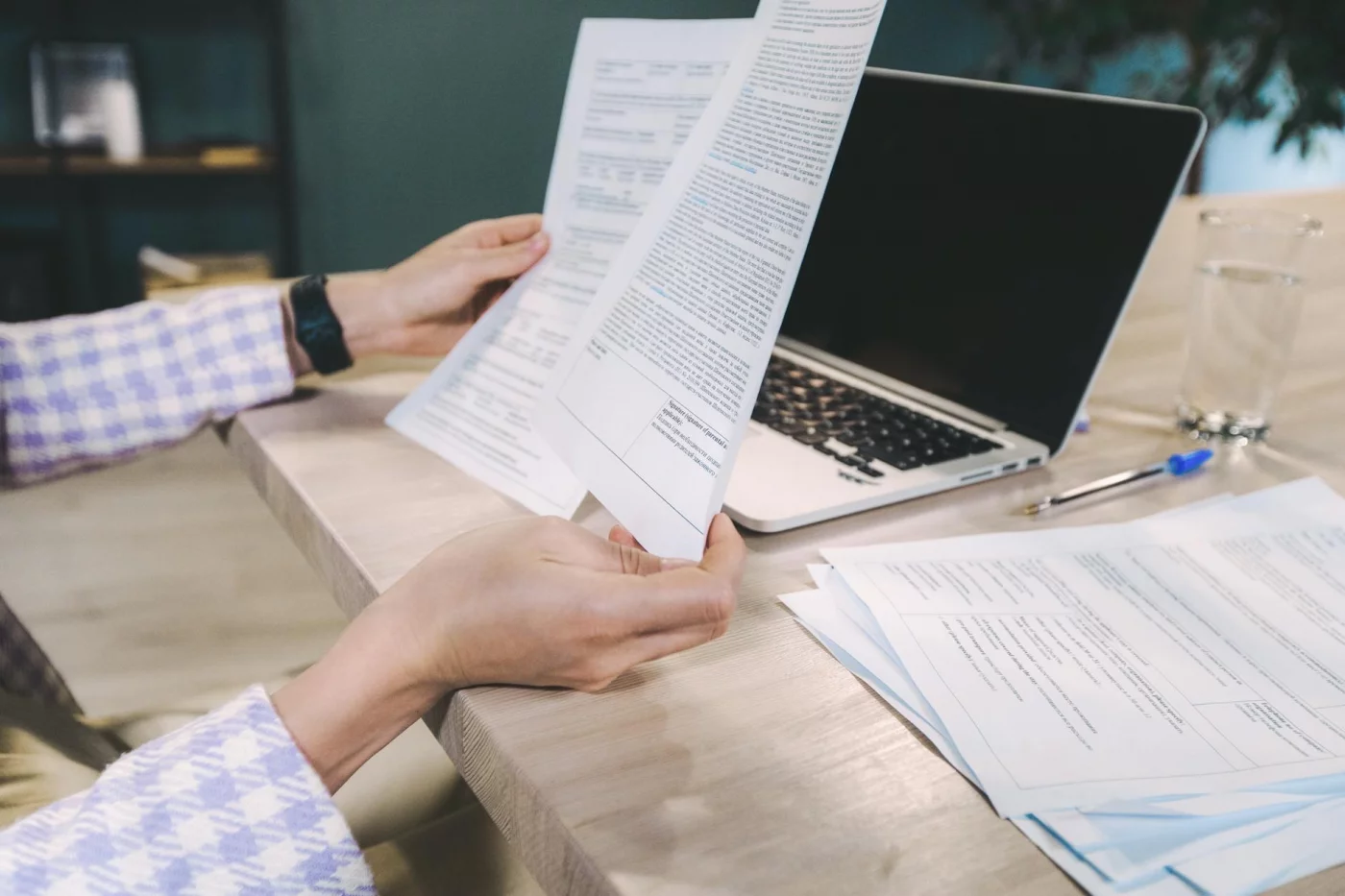 Hands reviewing printed research papers beside a laptop, showing how to read scientific papers quickly and critically