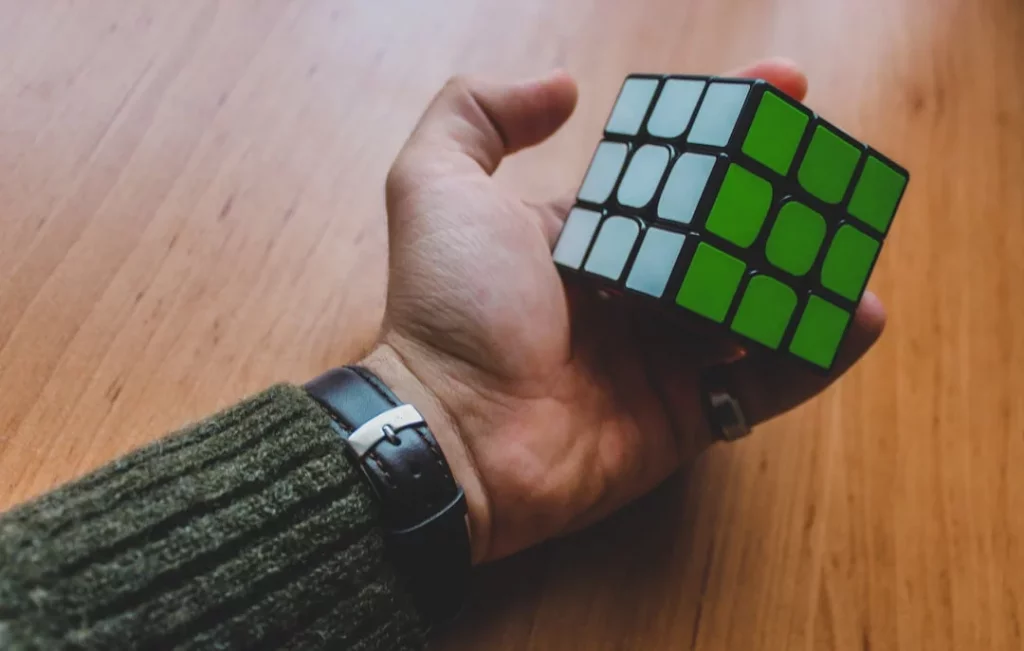 Hand holding a Rubik’s Cube on a wooden table to increase brain power in 7 minutes through skill practice