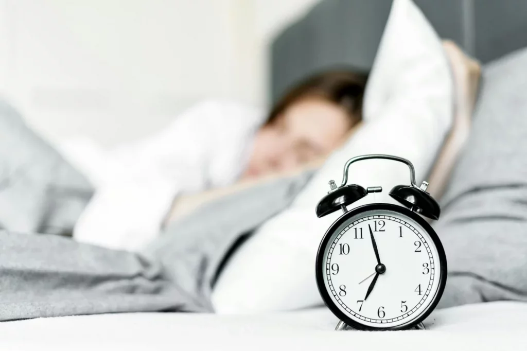 Retro alarm clock beside a sleeping woman, illustrating rem sleep and memory consolidation in a cozy bedroom