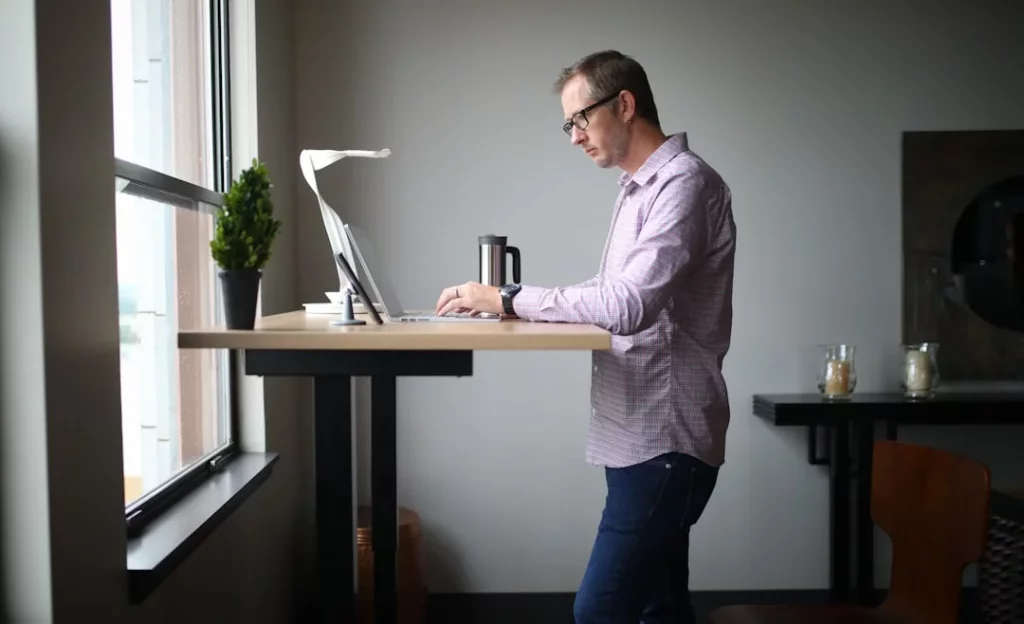 Man standing beside a wooden table in a brain-healthy workstation article about what is the 20 8 2 rule