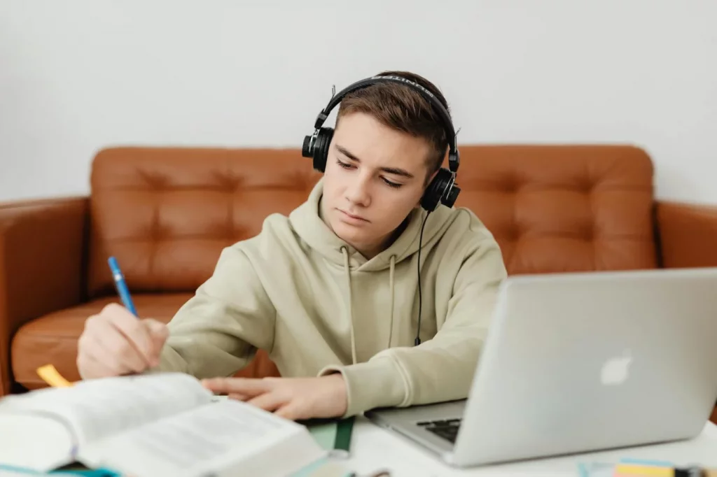 Teenage boy with headphones studying on a laptop, showing what music should you listen to while studying