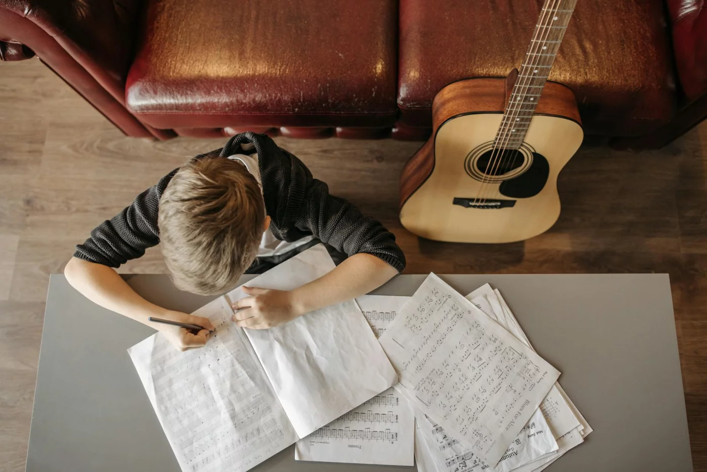 Child writing music notes at home with a guitar, exploring what music should you listen to while studying